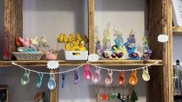 A shelf displays several Easter-themed handmade products such as crochetted bunnies and chickens. There are also colourful bunny-shaped holders with Easter eggs in them. A price sticker is placed on the side of the shelf.